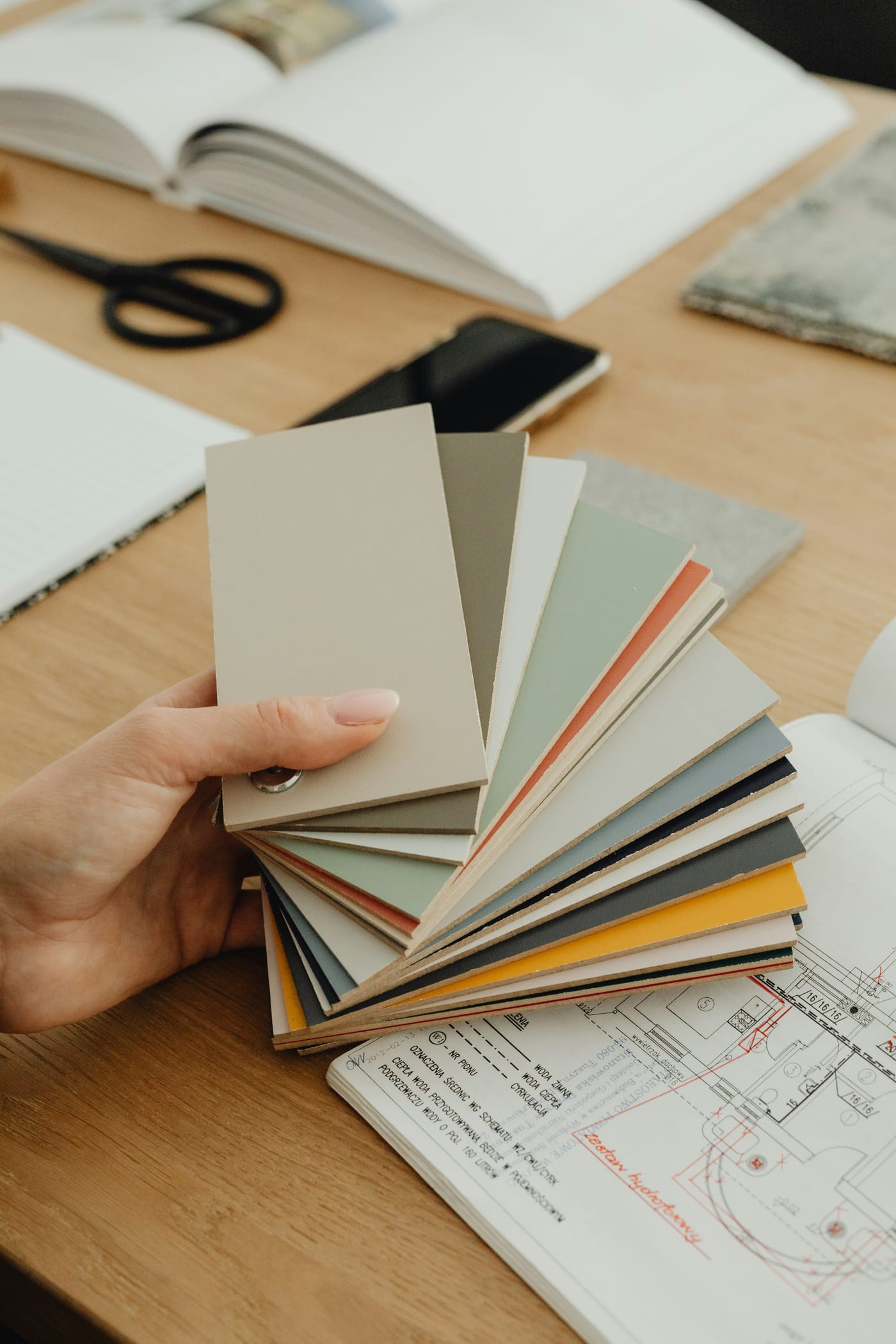 Mão segurando um leque de amostras de cores e materiais sobre uma planta de projeto de arquitetura