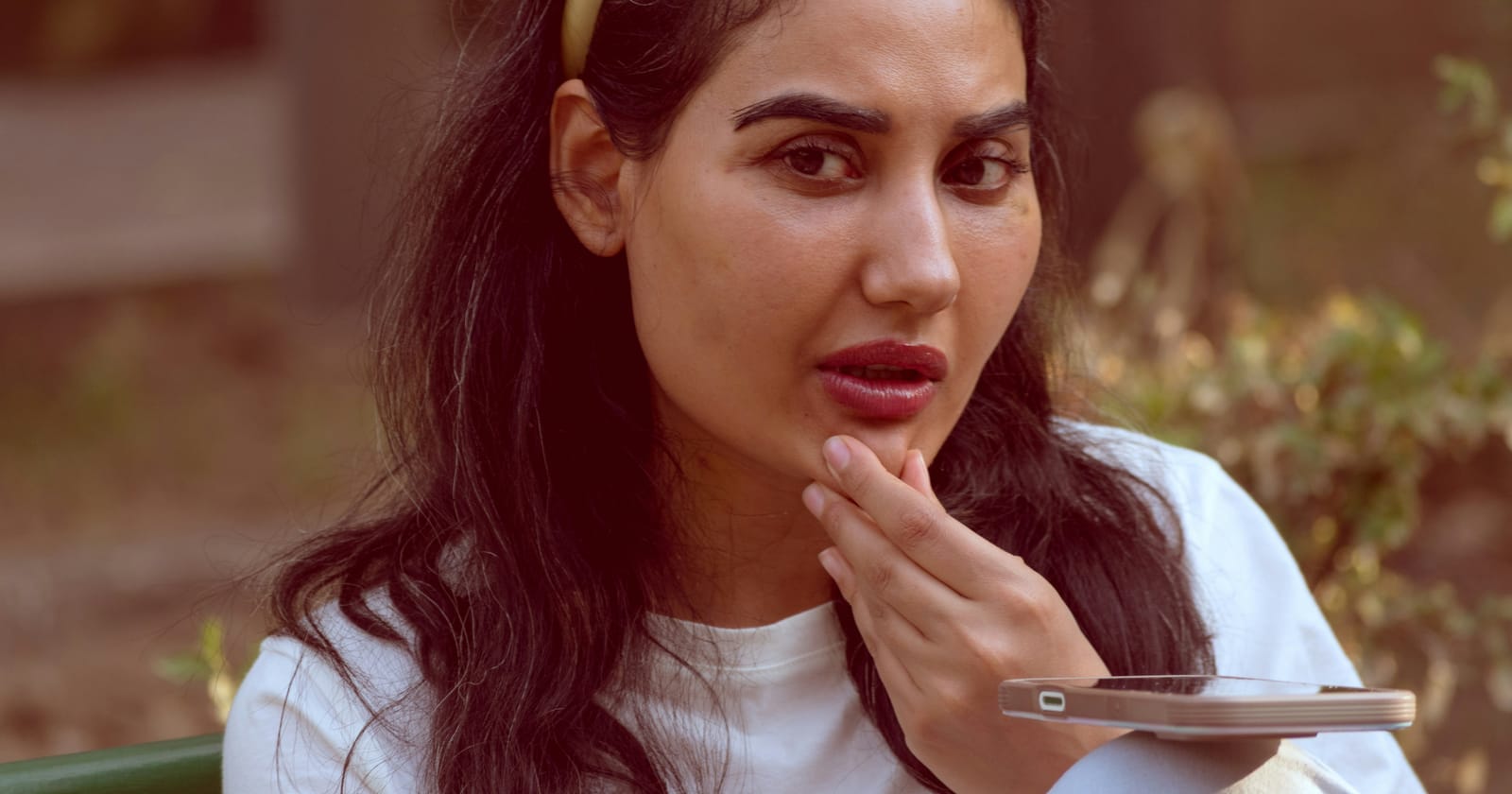 Mulher com expressão pensativa segurando o celular, comparando preço antes de entrar em contato com uma empresa