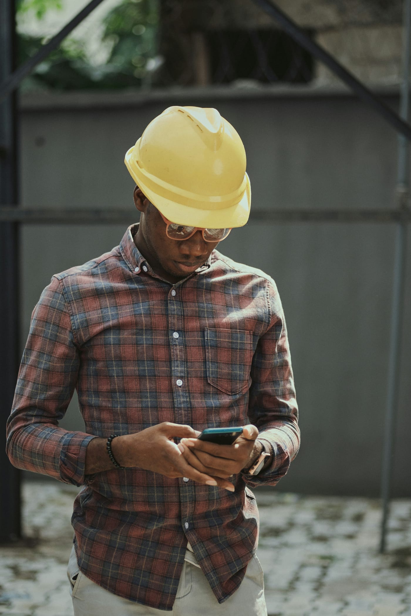 Engenheiro de capacete amarelo conferindo o celular em um canteiro de obra