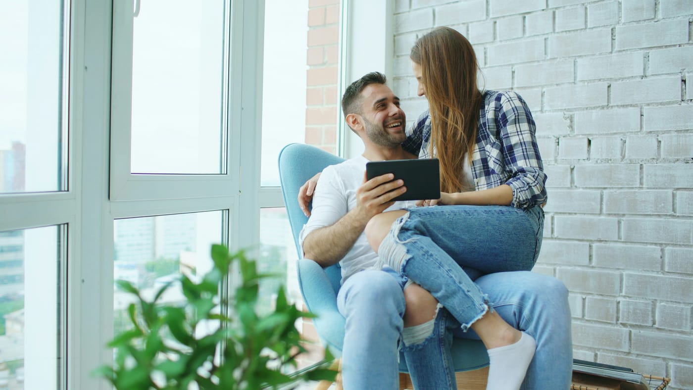 Casal sorridente conferindo informações num tablet antes de decidir uma compra