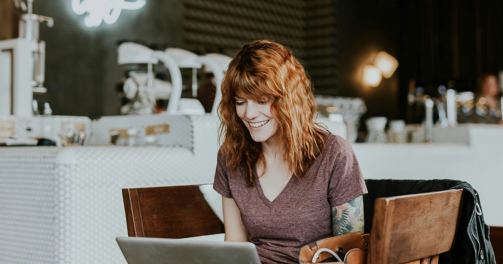 Mulher sorrindo em frente ao notebook em uma cafeteria, pesquisando informações antes de decidir uma compra