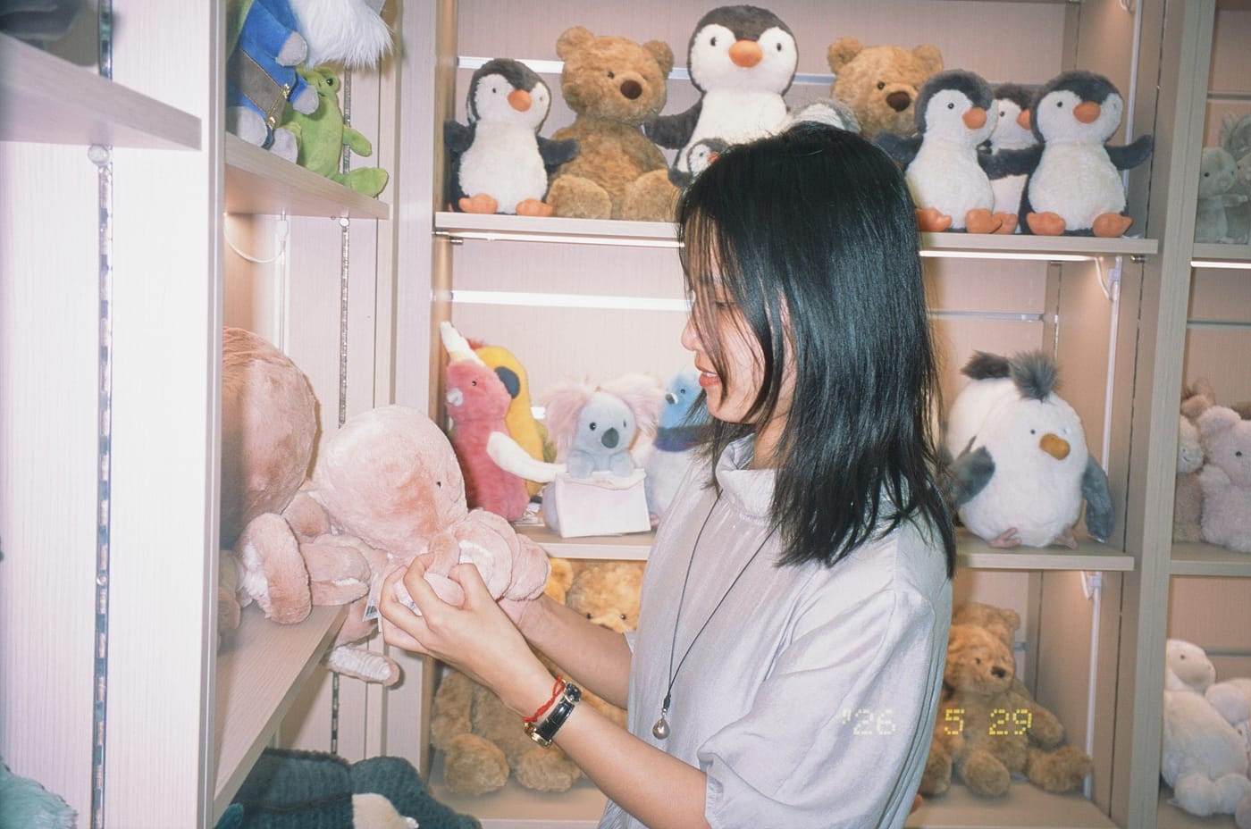 Mulher segurando e observando uma pelúcia numa prateleira de loja de brinquedos