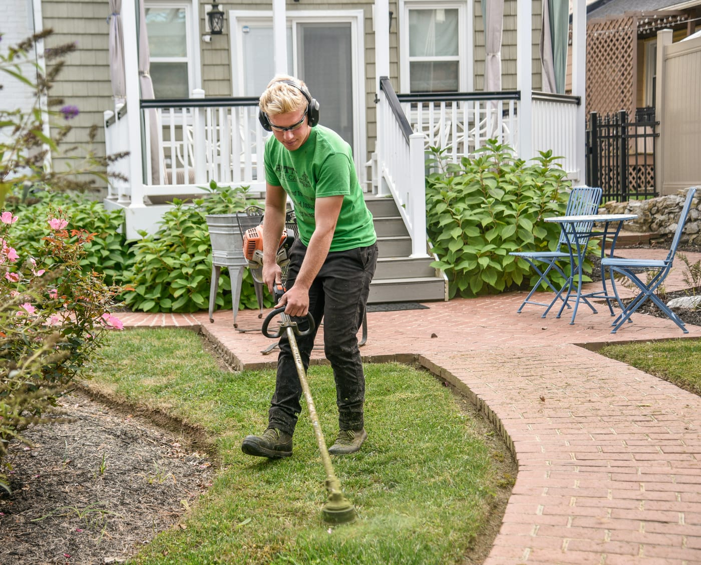 Profissional de paisagismo aparando grama em jardim residencial durante atendimento
