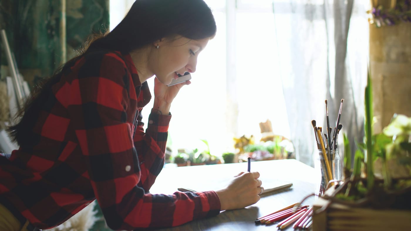 Atendente ao telefone anotando no caderno o pedido de um cliente indicado