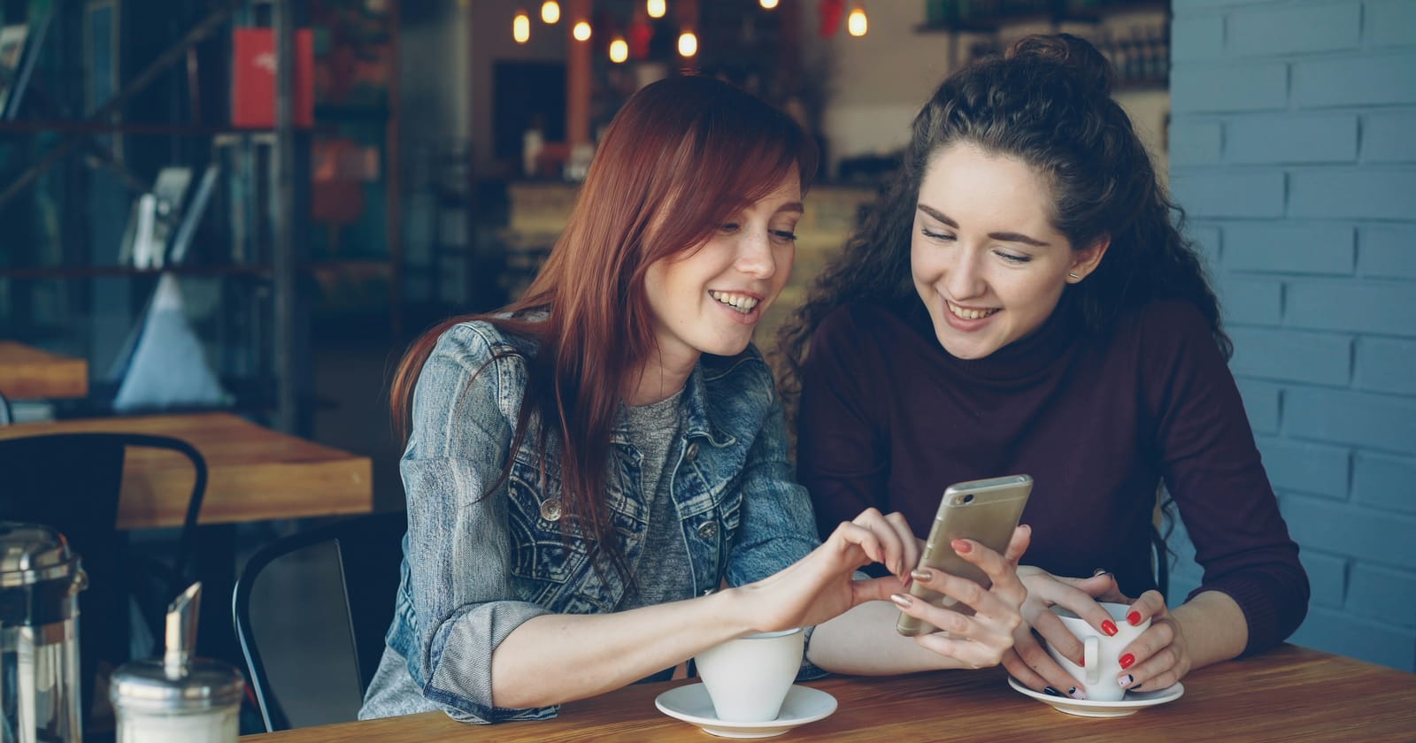 Duas amigas sorridentes conferindo no celular a indicação de uma empresa