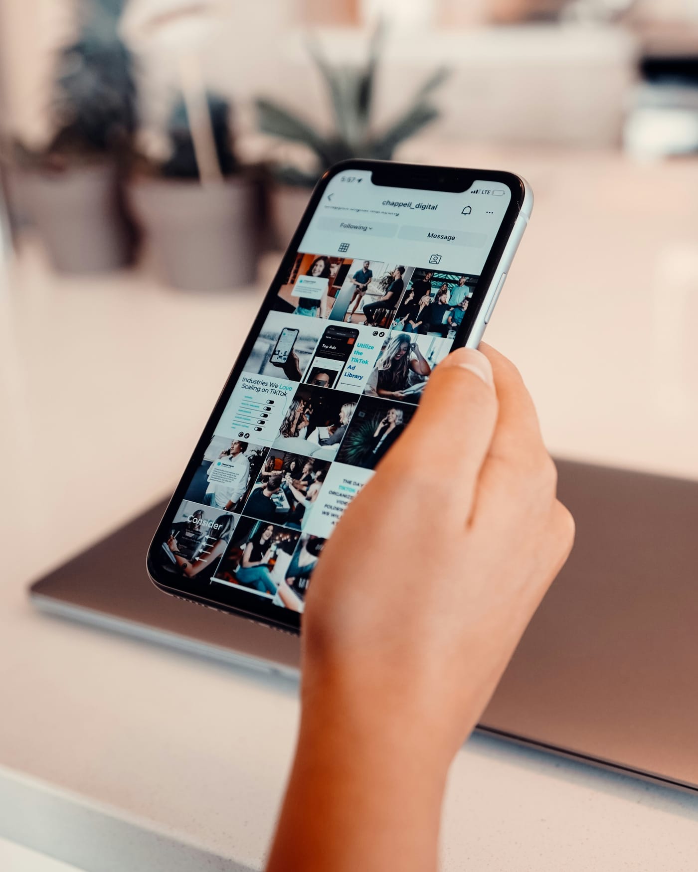 Mão segurando um celular com o perfil de uma empresa aberto no Instagram, mostrando fotos e vídeos de conteúdo comercial
