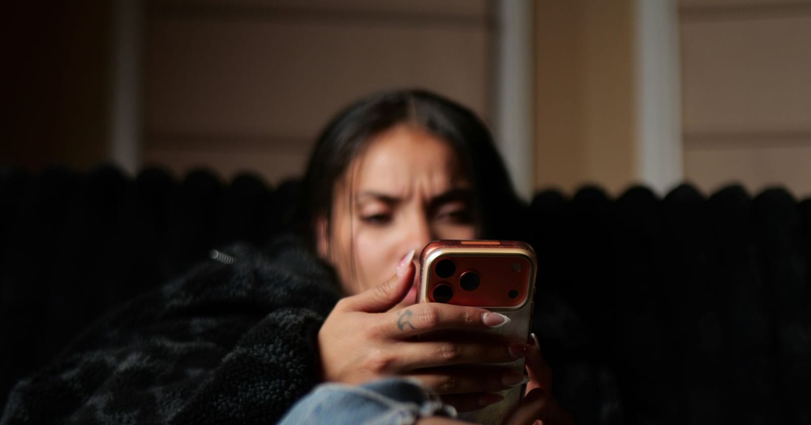 Mulher no sofá conferindo o celular à noite, pesquisando antes de fazer uma compra de madrugada