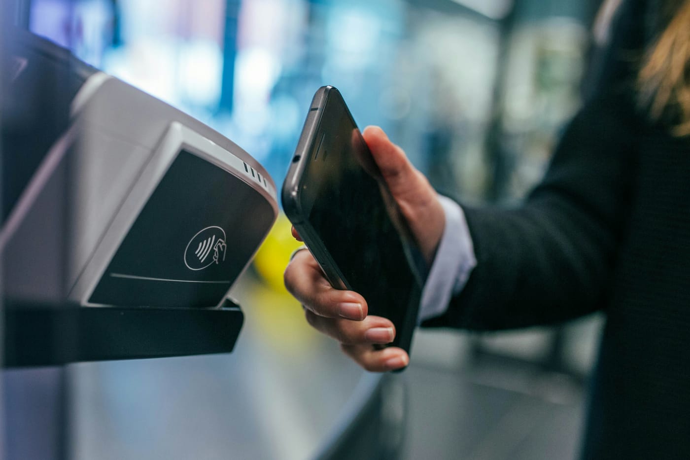 Mão segurando um celular próximo a uma maquininha de pagamento por aproximação