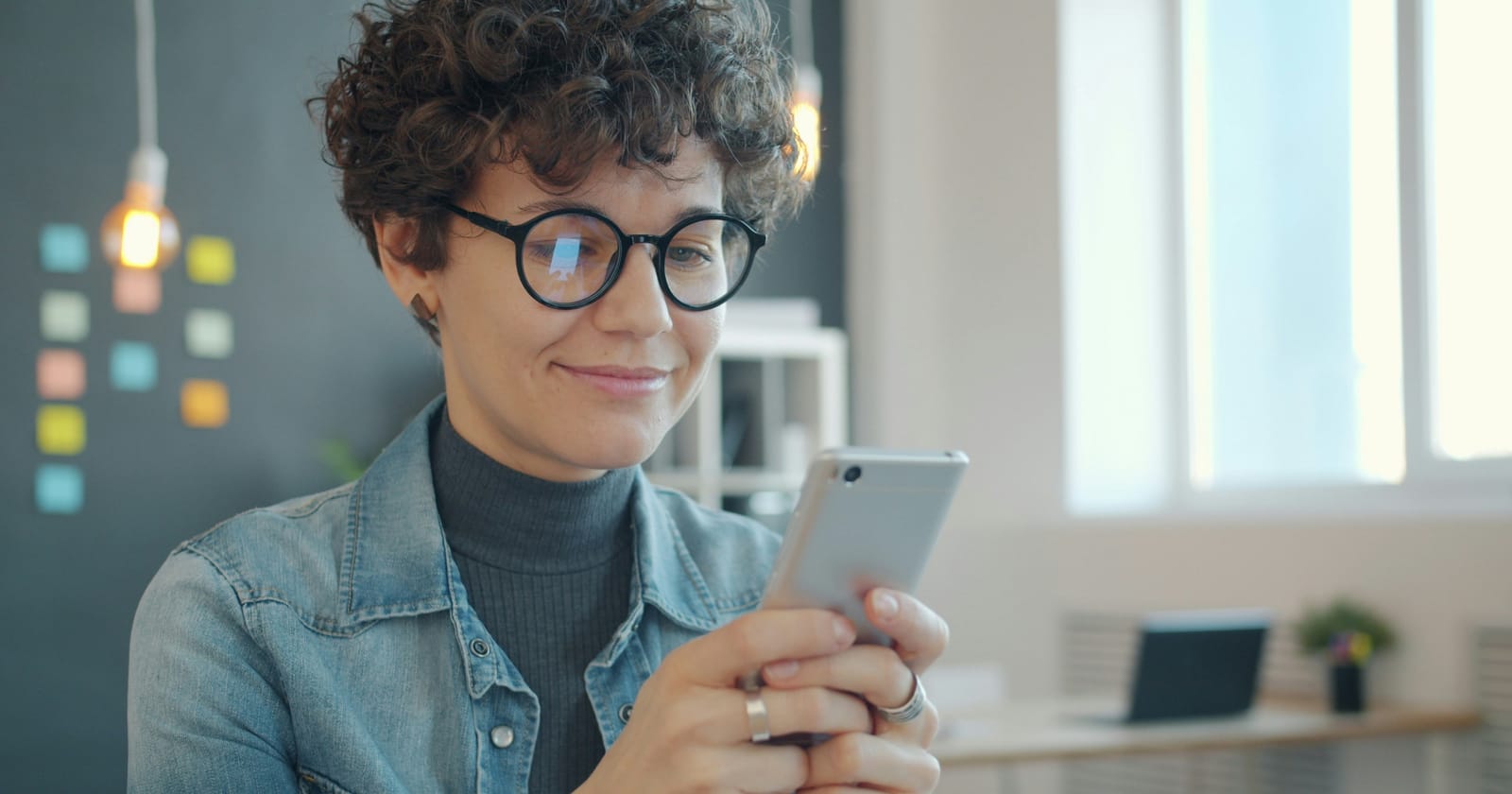 Mulher sorrindo enquanto responde mensagem no celular, representando o atendimento via WhatsApp Business