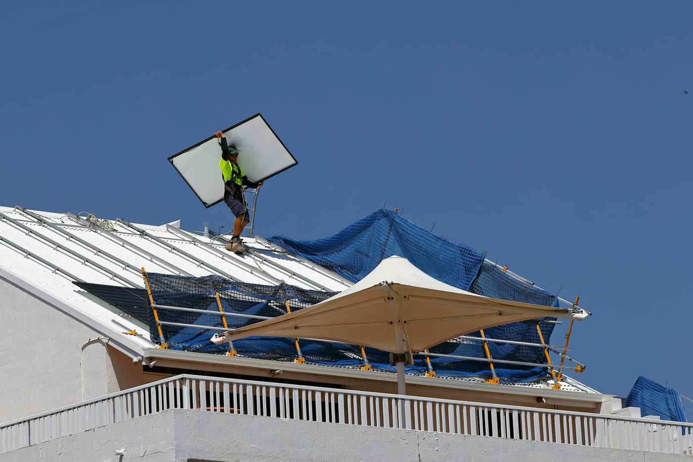 Técnico de uniforme instalando placa de energia solar no telhado de um prédio